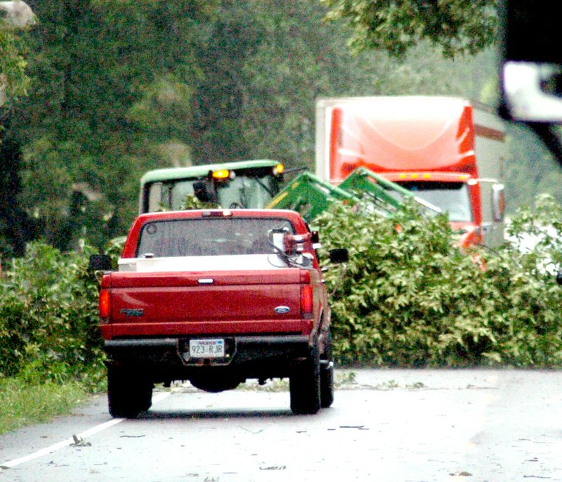 Photo by Mike Eckels A tractor pulls several large tree limbs off Arkansas Highway 12 near the Springtown Cemetery. The limbs fell across the highway during a violent windstorm July 23. Traffic was halted on the major thoroughfare between Gentry and Highfill for 45 minutes while local farmers and Highfill city workers cleared the debris.