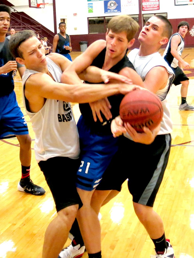 Photo by Mike Eckels A Rogers Mountie player gets caught in a Bulldog sandwich as Victor Urquidi (left) and Jay Porter (right) fight to gain possession of the basketball during the Rogers/Decatur game July 24 at the Gentry High School gym.