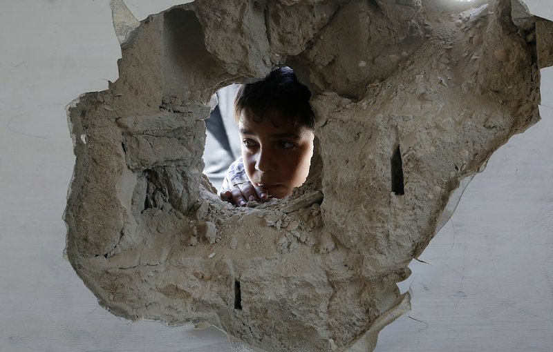 A boy looks through a hole on the wall made after an Israel strike at the Abu Hussein U.N. school in the Jebaliya refugee camp in the northern Gaza Strip on Wednesday, July 30, 2014. 