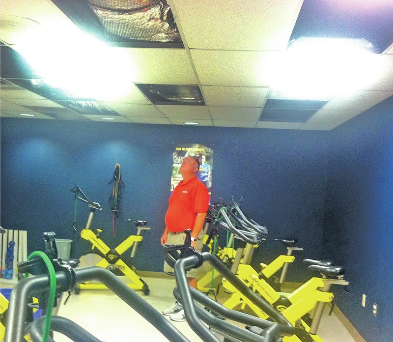 Staff Photo John Gore Rick Stocker, Rogers recreation director, surveys ceiling damage Thursday in the spinning room at the Rogers Activity Center. Water from heavy rain Wednesday spilled through from the roof, which was under repair, damaging ceilings on the second floor. Fitness classes were canceled Thursday, and the second floor was closed for cleanup.