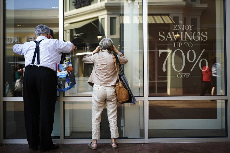 Shoppers Ron and Phyllis Crimm peek inside a Coach Inc. outlet store instead of waiting in line during a charity preview event on the eve of the grand opening of the Outlet Shoppes of The Bluegrass in Simpsonville, Kentucky, U.S., on Wednesday, July 30, 2014. Confidence among U.S. consumers retreated last week to an almost two-month low as limited wage growth chipped away at perceptions about personal finances, according to the Bloomberg Consumer Comfort Index. Even with the setback in sentiment, the weekly measure is holding close to its high of the year as a pickup in employment opportunities persists and stocks trade near a record. Photographer: Luke Sharrett/Bloomberg *** Local Caption *** Ron Crimm; Phyllis Crimm