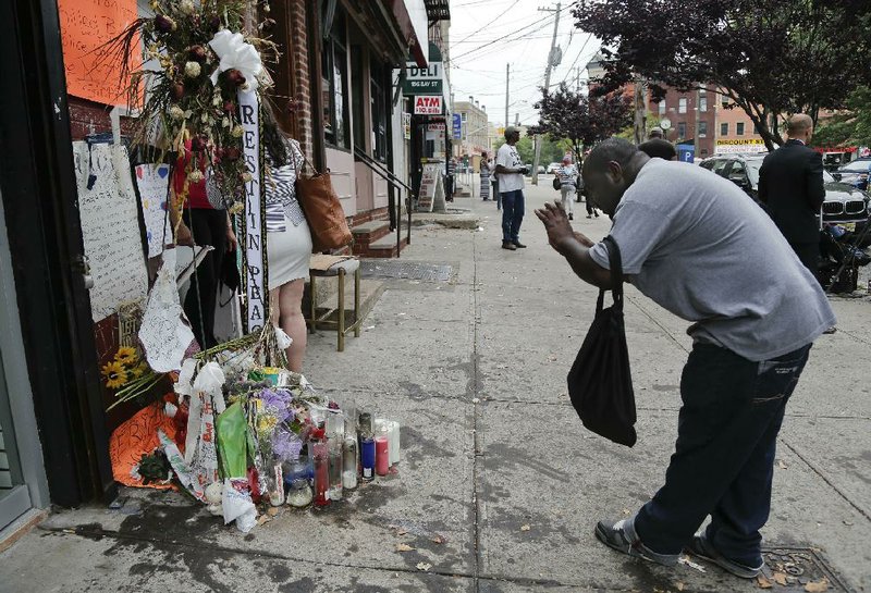 A passer-by stops to take a photo of a makeshift memorial for Eric Garner, Friday, Aug. 1, 2014, in the Staten Island borough of New York. Garner died after he was put in a chokehold while being arrested at the site last month for selling untaxed loose cigarettes. On Friday, the medical examiner ruled Garner's death to be a homicide caused by a police chokehold. (AP Photo/Julie Jacobson)  