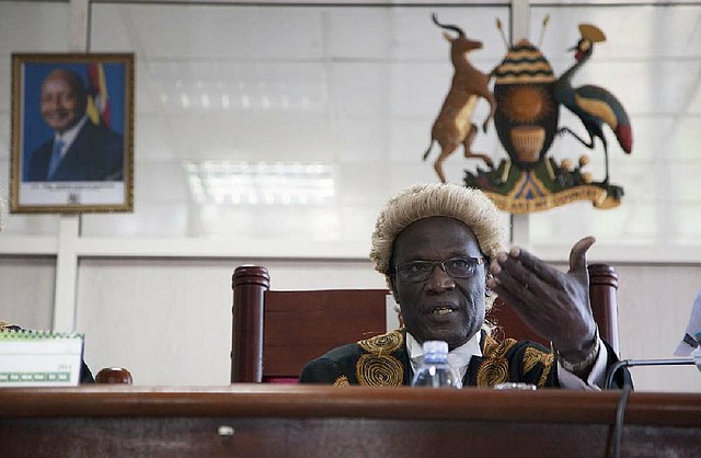 A photo of Uganda's president hangs on the wall, left, as Judge, Stephen Kavuma reads the verdict  at Uganda’s Constitutional court,  Friday, Aug.1, 2014. A Ugandan court has invalidated an anti-gay bill signed into law earlier this year, saying it was illegally passed and is therefore unconstitutional. The panel of five judges on the East African country's Constitutional Court said the speaker of parliament acted illegally when she went ahead to allow a vote on the measure despite at least three objections over lack of quorum. (AP Photo/Rebecca Vassie)