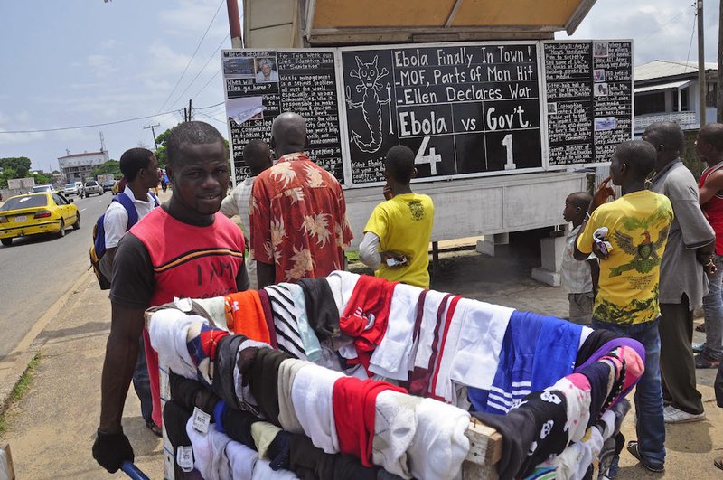 A man selling clothes walks past people reading the comments on current events in Liberia, including the deadly Ebola virus, written by social commentator Alfred Sirleaf, on a blackboard in Monrovia, Liberia, on Saturday Aug. 2, 2014. 