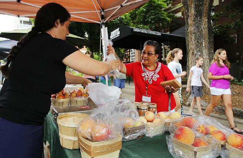 NWA Media/DAVID GOTTSCHALK - 7/24/14 - Lydia Astorga, grants and agreements specialist with the United States Department of Agriculture Risk Management Agency Risk Management Education Division, makes a purchase from Alex Munson from A and A Orchard of Green Forest Thursday July 28, 2014 at the Fayetteville Farmers' Market on the square in Fayetteville. Astorga is part of a group of high school and college students from across the country who represent American Indian tribes visiting  the market learning about nutrition as part of an inaugural summer program organized by the new Indigenous Food and Agriculture Initiative and the School of Law at the University of Arkansas.