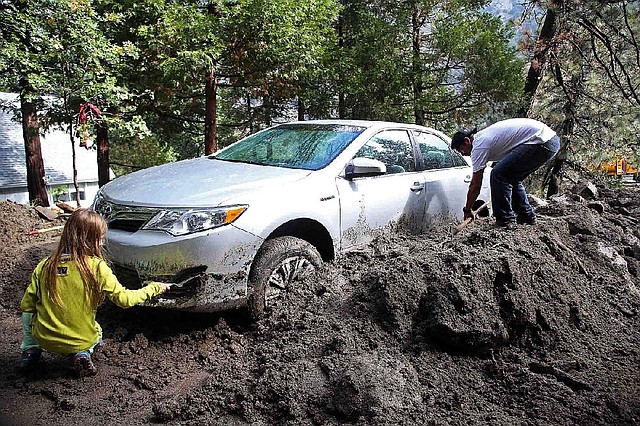 Andrew Watson and his daughter Taylor Becker dig out their car after rocks and mud inundated their home in the mountain community of Forest Falls in the San Bernardino Mountains Monday, Aug. 4, 2014. Crews cleared roads in an area where some 2,500 had been stranded after thunderstorms caused mountain mudslides in Southern California over the weekend, while authorities estimated that between 6 and 8 homes were badly damaged and likely uninhabitable. One person was found dead in a vehicle that was caught in a flash flood. A group of campers spent the night at a community center near Forest Falls headed. (AP Photo/Nick Ut)