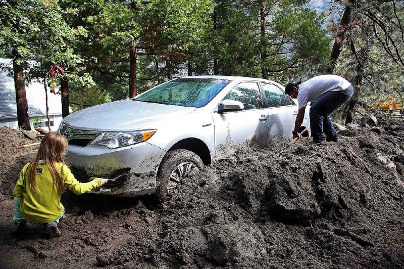 Andrew Watson and his daughter Taylor Becker dig out their car after rocks and mud inundated their home in the mountain community of Forest Falls in the San Bernardino Mountains Monday, Aug. 4, 2014. Crews cleared roads in an area where some 2,500 had been stranded after thunderstorms caused mountain mudslides in Southern California over the weekend, while authorities estimated that between 6 and 8 homes were badly damaged and likely uninhabitable. One person was found dead in a vehicle that was caught in a flash flood. A group of campers spent the night at a community center near Forest Falls headed. (AP Photo/Nick Ut)