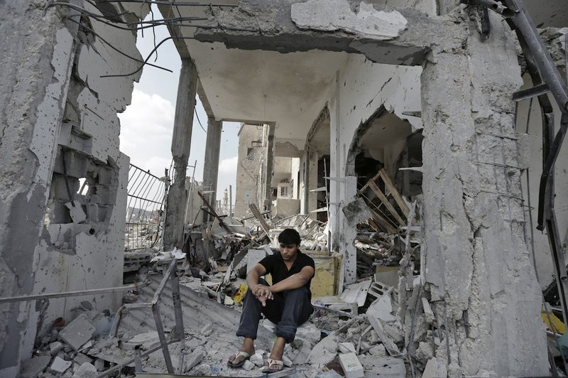 Palestinian Fadi Ehajela, 20, sits on the rubble of what used to be his family's supermarket on the ground floor of the Nada Towers at a residential neighborhood in the town of Beit Lahiya, northern Gaza Strip, on Tuesday, Aug. 5, 2014. The supermarket which staffed ten people and his nearby family home were destroyed in an Israeli strike, according to Ehajela. The family have now found refuge in a U.N. school as thousands of other Palestinians.