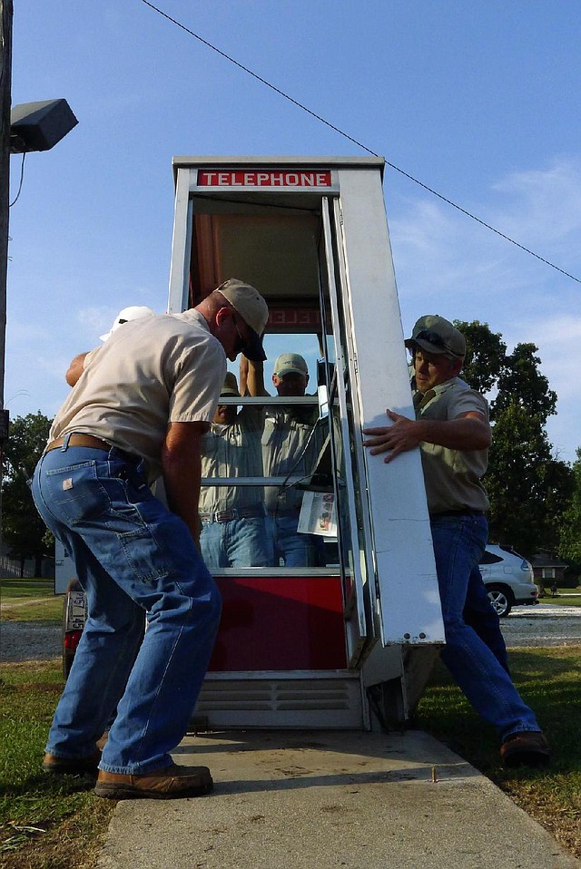 Workers for the Prairie Grove Telephone Co. put the phone booth back in place Tuesday in front of the Colonial Motel, where it had sat since 1959 until it was knocked down by an SUV on June 7. 