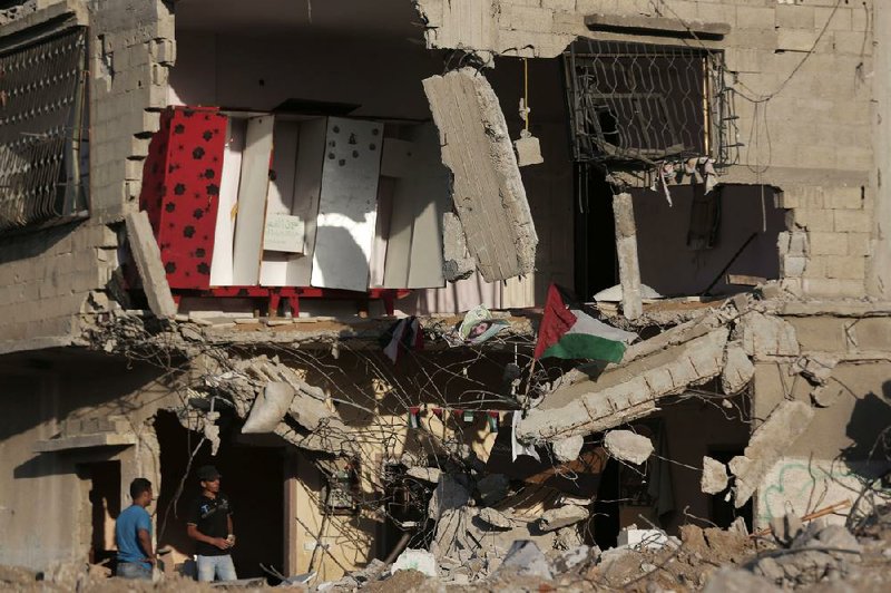 Palestinians stand amid debris after they salvaged belongings, as the national flag flies on the rubble of the house, destroyed by an Israeli strike in the Gaza City neighborhood of Shijaiyah, Gaza Strip, Thursday, Aug. 7, 2014. (AP Photo/Lefteris Pitarakis)