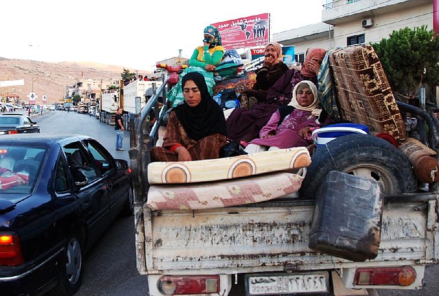Syrian refugees flee from the Lebanese eastern town of Arsal on their way to cross back into Syria, as they ride in the back of a pickup truck with their belongings at the Lebanese border crossing point of Masnaa, eastern Bekaa Valley, Lebanon, Thursday, Aug. 7, 2014. Up to 150 cars packed with Syrian refugees were seen leaving Arsal. A security official in eastern Lebanon said arrangements were made for them to cross back into Syria through the border crossing. It was not immediately clear where in Syria the refugees were going, but many may have been fleeing the violence in Arsal for areas inside their country where there has been less fighting recently. (AP Photo)