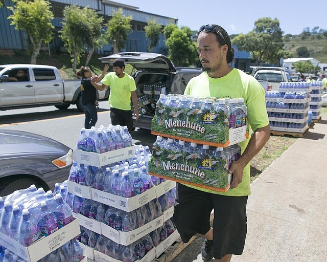 A worker at the Menehune Water Company carries bottle of water to waiting customers, Thursday, Aug. 7, 2014, in Aiea, Hawaii.  Hawaii is bracing for two back to back hurricanes, Iselle and Julio, which are on course to hit the Islands.  Bottles of water are quickly disappearing off shelves in Hawaii causing many people to line up for several hours to purchase water directly from the company.  (AP Photo/Marco Garcia)