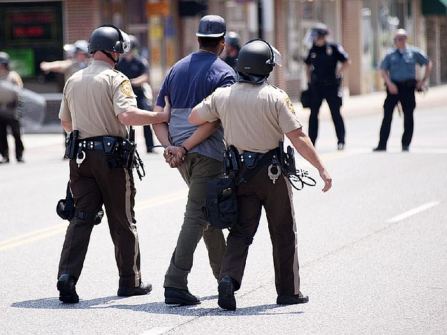 Police detain a protester following a  march along Florissant Road in downtown Ferguson, Mo. Monday, Aug. 11, 2014. The group marched along the closed street, rallying in front of the town's police headquarters to protest the shooting of 18-year-old Michael Brown by Ferguson police officers. Brown, who was killed in a confrontation with police in the St. Louis suburb, was shot Saturday, Aug. 9, 2014, and died following the confrontation with police. (AP Photo/Sid Hastings)