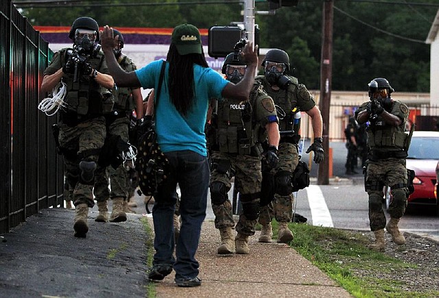 Police in riot gear walk toward a man with his hands raised Monday in Ferguson, Mo. Authorities have made several arrests in Ferguson, where crowds have looted and burned stores, vandalized vehicles and taunted police after a vigil for an unarmed black man who was killed by police.