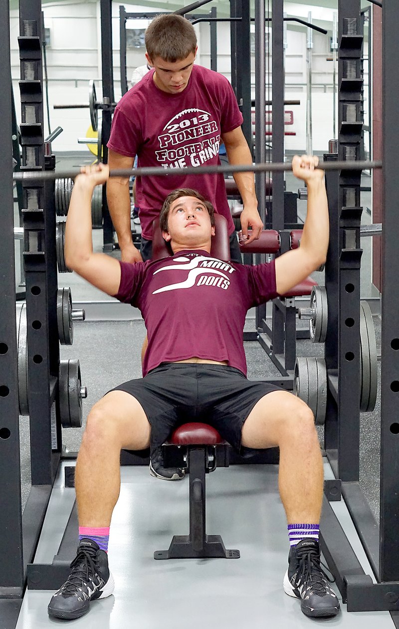 Photo by Randy Moll Gentry senior Jon Brown lifts weights, with Phillip Montgomery spotting, during practice in the Pioneer Activities Complex on Aug. 6. The weightlifting time was a part of football practice for members of the Pioneer football squad.
