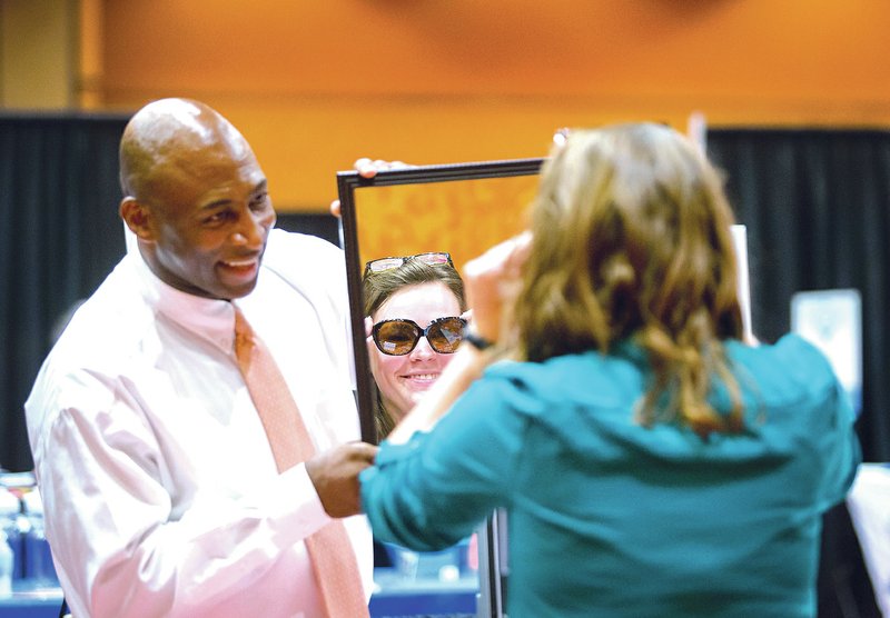 STAFF PHOTO JASON IVESTER Chuck Washington, left, with In-N-Out Screening Services holds a mirror Tuesday while Lana Hackler of Fayetteville tries on a pair of sunglasses at his booth during the NWA Business Expo at the John Q. Hammons Center in Rogers. The event, hosted by the Rogers-Lowell Area Chamber of Commerce, featured businesses from across the region showcasing their products/services as well as seminars.