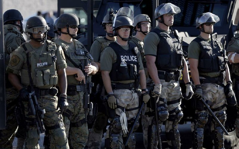 Police in riot gear watch protesters Wednesday in Ferguson, Mo. “We went through some pretty bad areas of Afghanistan, but we didn’t wear that much gear,” said Kyle Dykstra, an Army veteran and former security officer for the State Department.