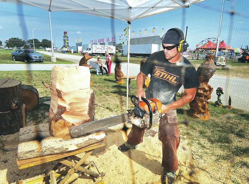 STAFF PHOTO BEN GOFF &#8226; @NWABenGoff Brandon Adams of Adams Chainsaw Art and Sawmill in Mount Vernon, Mo., carves a bear Friday in his booth at the Benton County Fair near Bentonville.