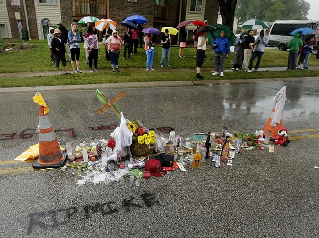 People gather next to a makeshift memorial for Michael Brown Saturday, Aug. 16, 2014, located at the site where Brown was shot by police a week ago in Ferguson, Mo. Brown's shooting in the middle of a street following a suspected robbery of a box of cigars from a nearby market has sparked a week of protests, riots and looting in the St. Louis suburb. (AP Photo/Charlie Riedel)