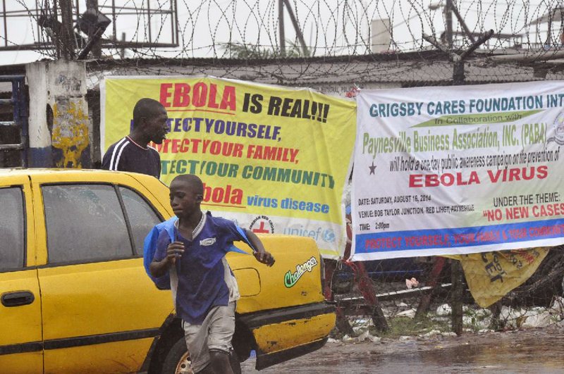 People pass by Ebola virus health warning signs, in the city of Monrovia, Liberia, Sunday, Aug. 17, 2014. Liberian officials fear Ebola could soon spread through the capital's largest slum after residents raided a quarantine center for suspected patients and took items including blood-stained sheets and mattresses. The violence in the West Point slum occurred late Saturday and was led by residents angry that patients were brought from other parts of the capital to the holding center, Tolbert Nyenswah, assistant health minister, said Sunday. (AP Photo/Abbas Dulleh)