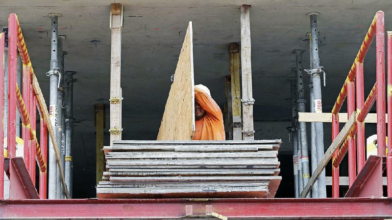 In this photo taken July 22, 2014, a construction worker carries a sheet of plywood at the site of a 36-floor high rise condominium in Miami. The National Association of Home Builders reports on sentiment among U.S. builders on Monday, Aug. 18, 2014. (AP Photo/Alan Diaz)