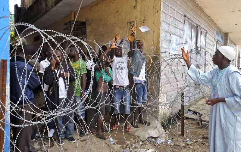 An aid worker tosses a water bag Friday to people cordoned off in a slum in Monrovia, Liberia. The government was delivering rice to the 50,000 sealed in there to contain Ebola.