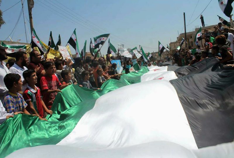 Anti-government protesters carry posters and a giant Syrian revolution flag Friday in Idlib province. The death toll from three years of Syria’s civil war has risen to 191,369, the United Nations reported Friday.