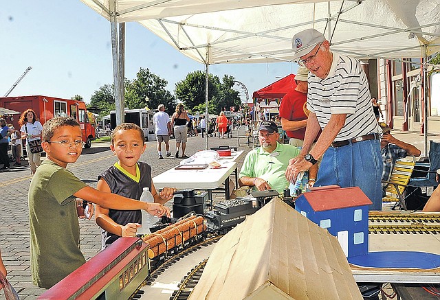 STAFF PHOTO FLIP PUTTHOFF Devante Battles, 8, and his brother, Jaheim Battles, 7, work model trains with the help of Bill Merrifield, right, on Saturday Aug. 23 2014 during the Frisco Festival in downtown Rogers. The trains were set up under tents staffed by Boston Mountain chapter of the National Railway Historical Society members. The boys took in the festival with their mom, Arrie Battles of Rogers.