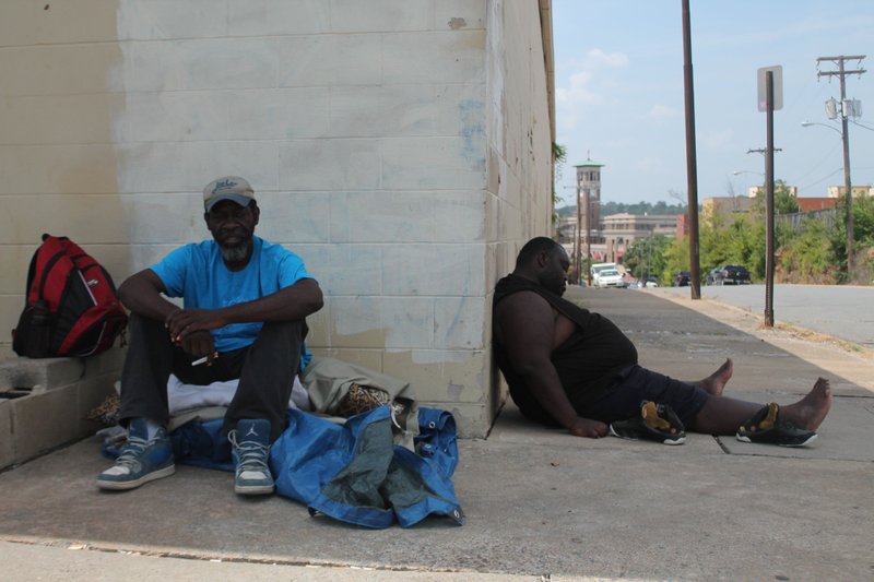 Two homeless men sit in the heat at the corner of West Markham and South Cross streets, unaware of an open cooling center directly across from them. 