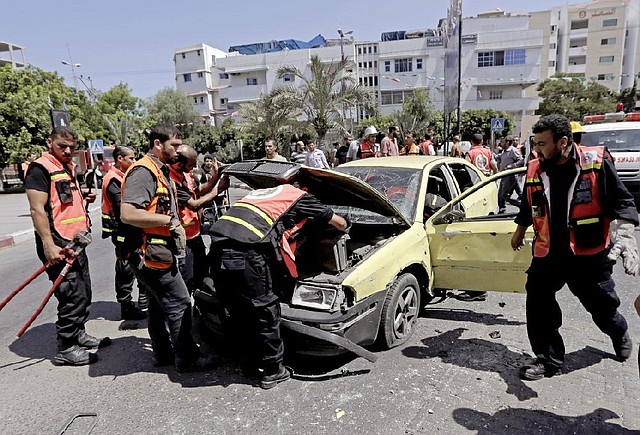 Palestinian firefighters inspect the wreckage of a vehicle following an Israeli airstrike in Gaza City, northern Gaza Strip, Monday, Aug. 25, 2014. Three people were wounded in an airstrike on the car, according Gaza health official Ashraf al-Kidra. (AP Photo/Adel Hana)