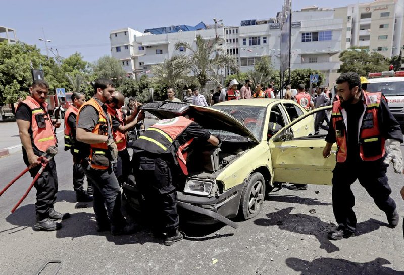 Palestinian firefighters inspect the wreckage of a vehicle following an Israeli airstrike in Gaza City, northern Gaza Strip, Monday, Aug. 25, 2014. Three people were wounded in an airstrike on the car, according Gaza health official Ashraf al-Kidra. (AP Photo/Adel Hana)