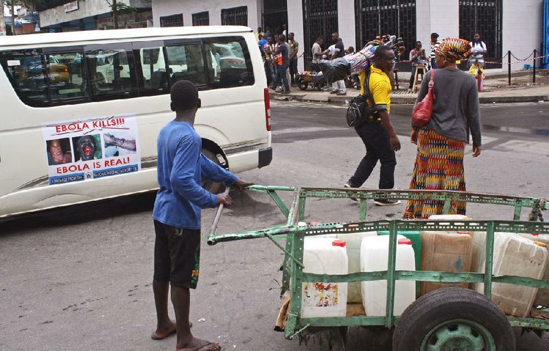 A water vendor, center, reads a warning on the door of a vehicle, left, regarding the deadly Ebola virus in Monrovia, Liberia, Tuesday, Aug. 26, 2014. The Ebola virus has the “upper hand” in an outbreak that has killed more than 1,400 people in West Africa, a top American health official has said, but experts have the tools to stop it.(AP Photo/Abbas Dulleh)