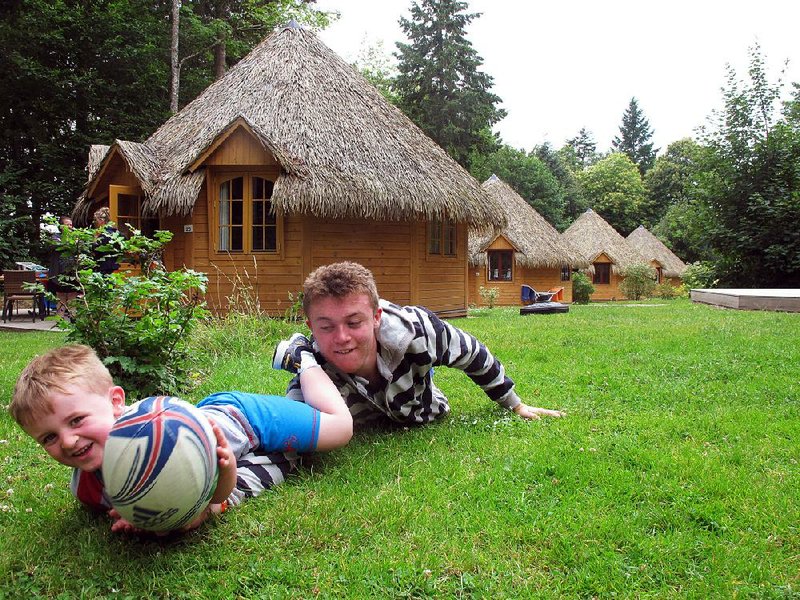 Sixteen-year-old David Pogatchnik and 4-year-old Harry Noble play rugby in front of a row of palm-frond-roofed cottages at the Domaine des Ormes campsite in Brittany, France. Some of the more luxurious cottages feature a full kitchen with dishwasher and microwave, bathroom with power shower, a choice of barbecues, and a deck for dining. Other accommodations at the camp include safari tents, mobile homes and tree houses.