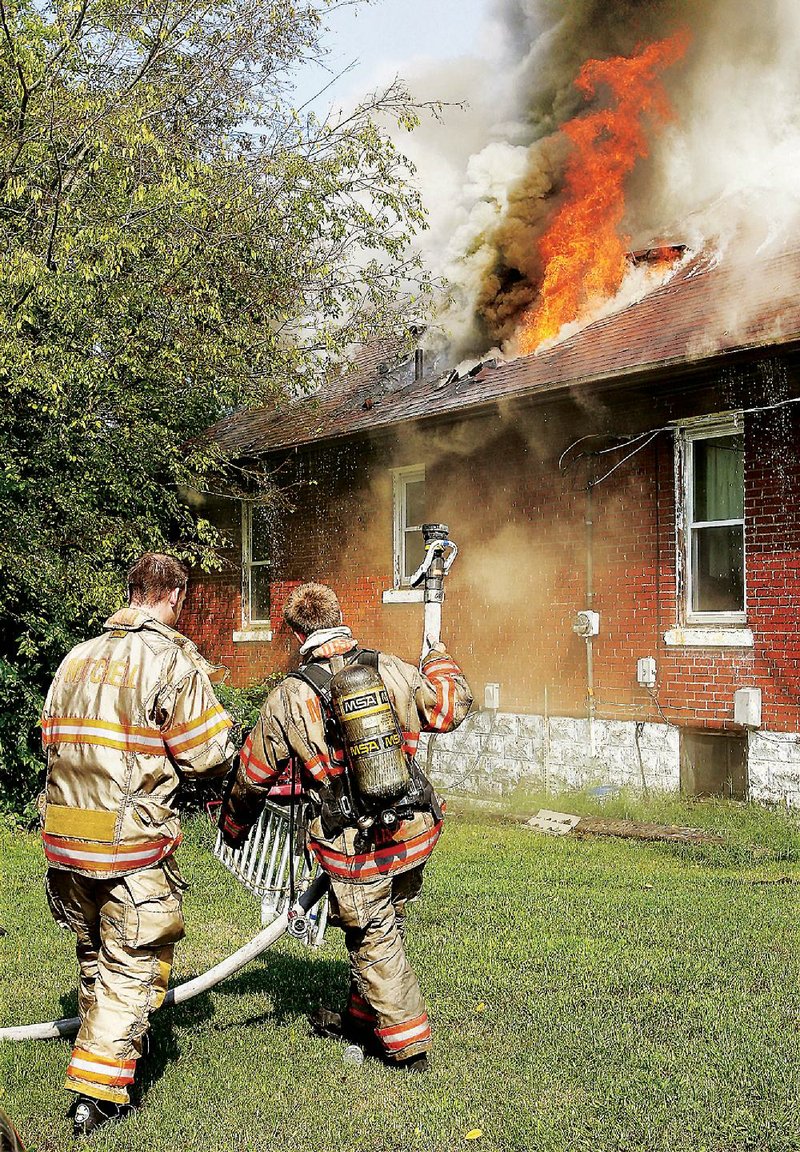 Firefighters move a hose line into place Thursday Aug. 28, 2014, in Mitchell, Ill., as flames shoot through the roof of the house which was gutted by the fire. A female occupant and her dogs were asleep in the house when the fire broke out but were able to escape through the smoke. Firefighters from Mitchell and South Roxana, Ill., with the eventual assistance of an aerial tower from the Madison, Ill., Fire Department, tried in vain to contain the flames which left little behind except the outside walls. No injuries were reported. (AP Photo/The Telegraph, John Badman) BELLEVILLE NEWS-DEMOCRAT OUT; ST. LOUIS POST-DISPATCH OUT