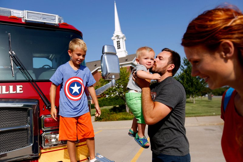 STAFF PHOTO JASON IVESTER Dan Fleming of Bentonville and his sons, Gavin, 8 (left) and Mason, 1, climb down from a truck of the Bentonville Fire Department after taking a tour. Bentonville firefighteres and other members of Benton County emergency services brought their equipment to the Northwest Arkansas Emergency Preparedness Fair on Aug. 23 at the Church of Jesus Christ of Latter-Day Saints in Bentonville. The equipment displays provided fun, in addition to education, for children at the fair.
