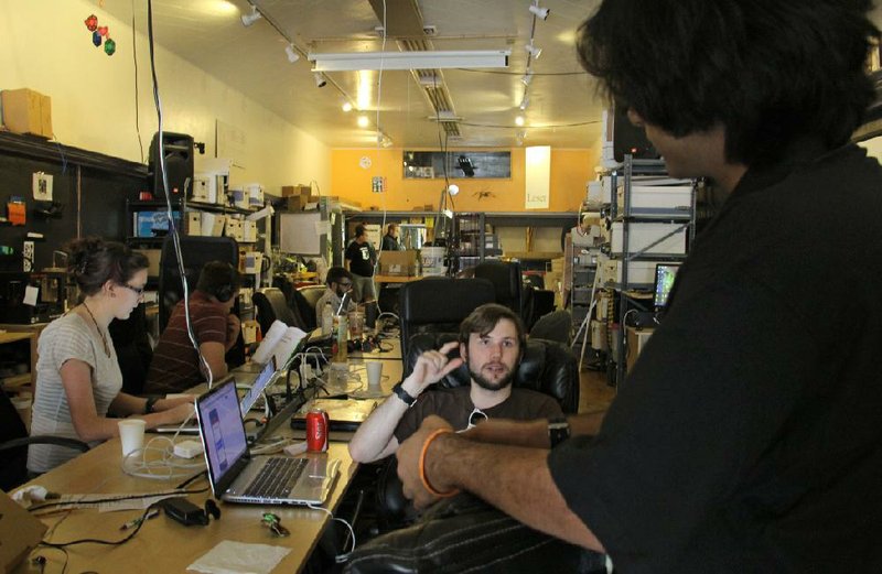 People talk and work on computers at a communal workbench at HeatSync Labs in Phoenix, in this photo made Wednesday, July 23, 2014. The nondescript garage-like workshop nestled between restaurants, a flower shop and jewelry stores offers a space where inventors and tinkerers can work on projects and share ideas. (AP Photo/Emaun Kashfi)