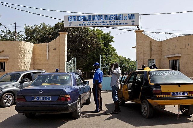 In this photo taken on Friday, Aug. 29, 2014,  a security guard, center left,  working at the University Hospital Fann, speaks to people inside a car, as a  man is  treated for symptoms of the Ebola virus inside the Hospital in Dakar, Senegal. The effort to contain Ebola in Senegal is “a top priority emergency,” the World Health Organization said Sunday, as the government continued tracing everyone who came in contact with a Guinean student who has tested positive for the deadly disease in the capital, Dakar. (AP Photo/Jane Hahn)