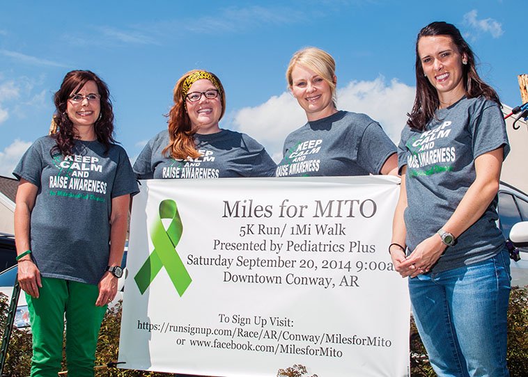 Alisha Holloway, from left, Caitlin Fitch, Kerri Hooten and Morgan Henry stand by a banner promoting the Miles for Mito 5K/1K race/walk on Saturday to support the United Mitochondrial Disease Foundation. Holloway, who lives in Vilonia, has mitochondrial disease, as do her two sons and two foster children. The race is being held to raise awareness of the disease, as well as money.