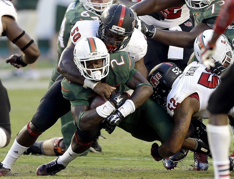 Miami running back Joseph Yearby (2) is tackled by Arkansas State defensive lineman Tyler Gilbertson (50) and linebacker Quanterio Heath (52) in the second half of an NCAA college  football game in Miami Gardens, Fla., Saturday, Sept. 13, 2014. (AP Photo/Alan Diaz)