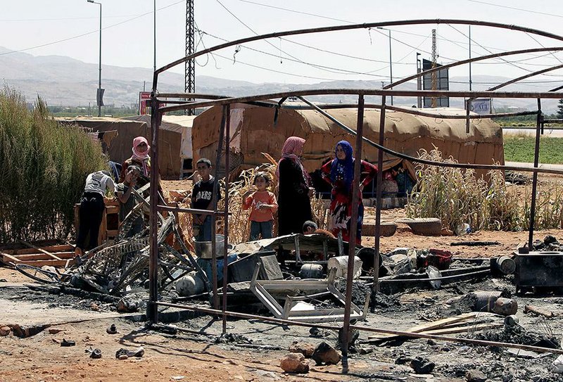 In this photo taken Wednesday, Sept. 10, 2014, displaced Syrian who fled their home in their country stand near tents that were burned by gunmen at a Syrian refugee camp in the village of Brital in the eastern Bekaa Valley, Lebanon. Syrians like them are becoming victims of a wave of revenge attacks carried out after one of several Lebanese soldiers captured by militants from Syria in a cross-border raid was beheaded by jihadists earlier this month. The killing of the Shiite soldier by Sunni extremists has aggravated sectarian tensions in Lebanon, which is bitterly divided over the war in neighboring Syria. (AP Photo/Bilal Hussein)