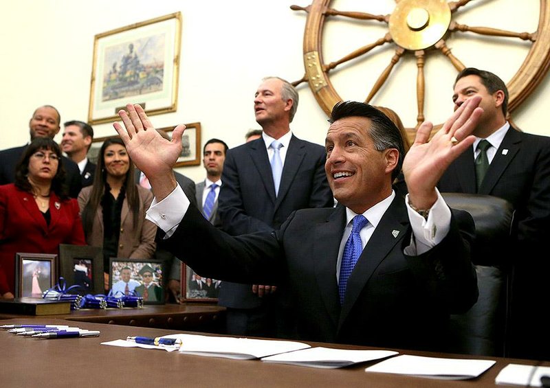 Surrounded by lawmakers and staff members, Nevada Gov. Brian Sandoval signs into law an unprecedented package of incentives to bring Tesla Motors' $5 billion battery factory to the state, at the Capitol, in Carson City, Nev., on Thursday, Sept. 11, 2014. (AP Photo/Cathleen Allison)