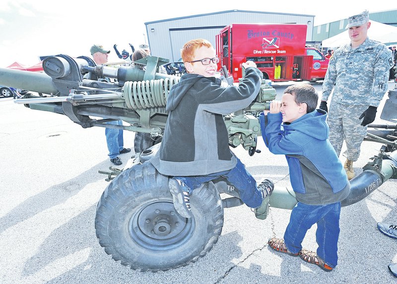 STAFF PHOTO ANDY SHUPE Brayden Miller, 9, left, and his brother Colson Miller, 8, check out the sighting mechanism of a 105mm Howitzer on display Saturday as Sgt. Charley Long of the Army National Guard Bravo Battery, 1st Battalion, 206th Field Artillery Regiment in Rogers watches during Sheep Dog Impact Assistance&#8217;s fourth annual Patriot Day at the Bentonville Airport. The event featured equipment and representatives from local agencies as a way to honor those who lost their lives in the Sept. 11, 2001, terrorist attacks and those who serve in law enforcement, the military, as firefighters and as emergency medical technicians.