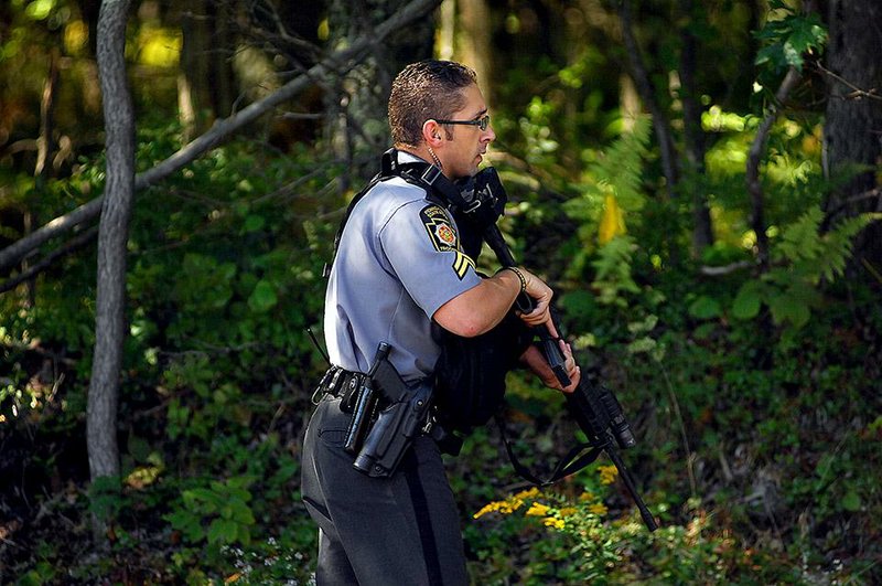 A Pennsylvania State Trooper walks into a wooded area as investigators on Sunday return to scour the woods across the street from the state police barracks on Sunday, Sept. 14, 2014, in Blooming Grove Township, Pa. On Friday night, State Trooper Cpl. Bryon Dickson, 38, of Dunmore, Pa.,was killed and Trooper Alex T. Douglass, 31, of Olyphant, Pa., was wounded after a shooting ambush at the barracks. No arrests have been made yet.  (AP Photo/The Scranton Times-Tribune, Butch Comegys)  WILKES BARRE TIMES-LEADER OUT; MANDATORY CREDIT