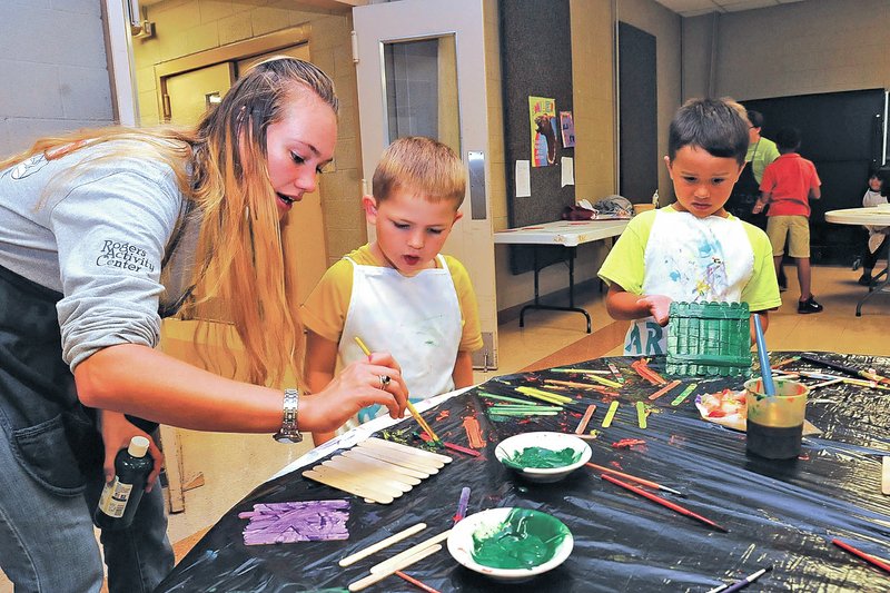 STAFF PHOTO FLIP PUTTHOFF Emily Young, from left, helps Dylan Akers and Conner Walker with a crafts project Friday at the Rogers Activity Center&#8217;s after-school program. Youngsters worked on two projects Friday afternoon.