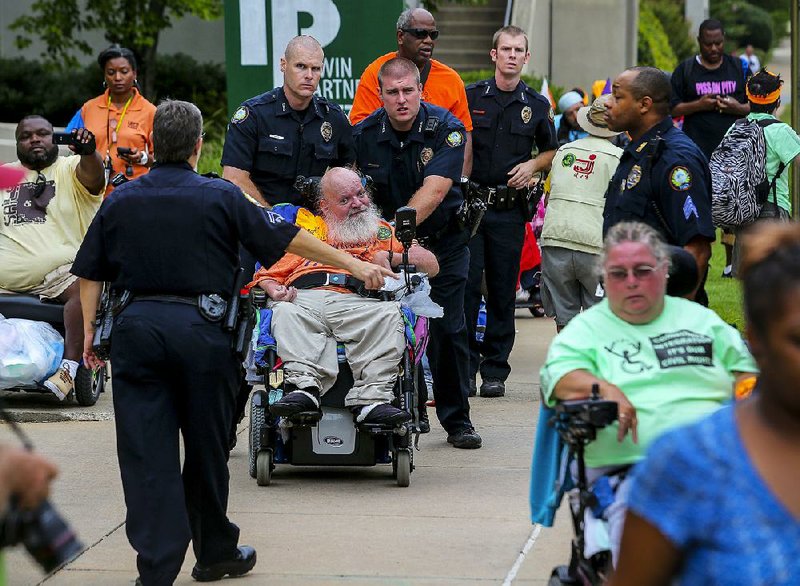 9/14/14
Arkansas Democrat-Gazette/STEPHEN B. THORNTON
Little Rock police wheel Rick James, of Lakewood, Colorado, center, to a wheelchair accessible CAT bus after arresting James and other activist, at right,  for trespassing inside the offices of the Arkansas Health Care Association and the Arkansas Assisted Living Association Monday in Little Rock.
