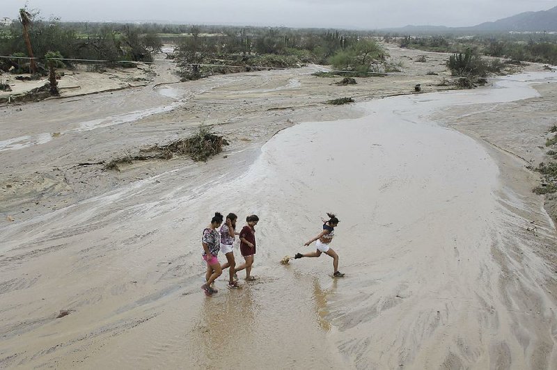 People cross a flooded creek in Los Cabos, Mexico, Monday, Sept. 15, 2014. Hurricane Odile hammered Mexico's Baja California Peninsula overnight, damaging homes and tearing away the facades of luxury resorts, shattering countless car and hotel windows and leaving lobbies swamped and full of debris on Monday. (AP Photo/Victor R. Caivano)