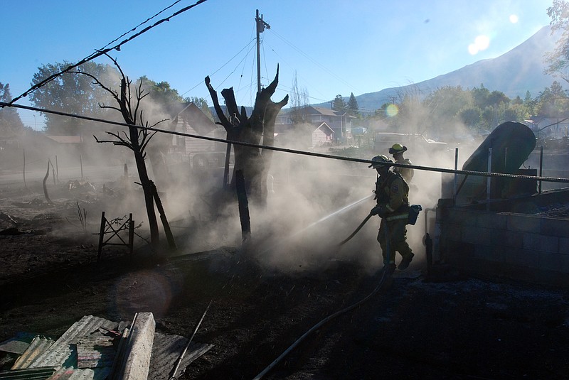 The Associated Press FIRE DAMAGE: Firefighters hose down the smoldering remains of a home Tuesday in Weed, Calif. A fast-moving wildfire destroyed at least 100 structures before winds died down and firefighters got a line around most of the fire.