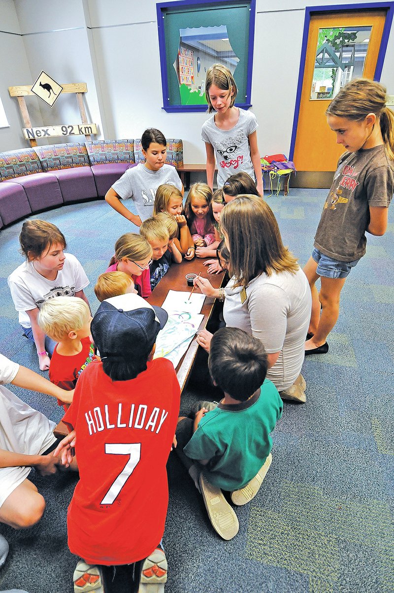 STAFF PHOTO J.T. Wampler Children gather around Joy Poynor while she demonstrates painting at the Rogers Public Library.