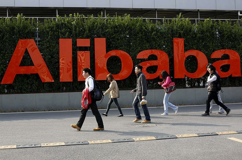 FILE - In this March 17, 2014 file photo, people walk past a company logo at the Alibaba Group headquarters in Hangzhou, in eastern China's Zhejiang province. Alibaba Group’s U.S. stock offering is a wakeup call about an emerging wave of technology giants in China’s state-dominated economy. Until now, Chinese companies that made a splash in global stock markets were state-owned banks and oil companies. But they are big by decree, not because they sell products customers want. By contrast, private sector tech champions such as Lenovo Group in personal computers and search engine Baidu Inc. survived bruising competition to rise to the top of their industries. (AP Photo/File)  CHINA OUT