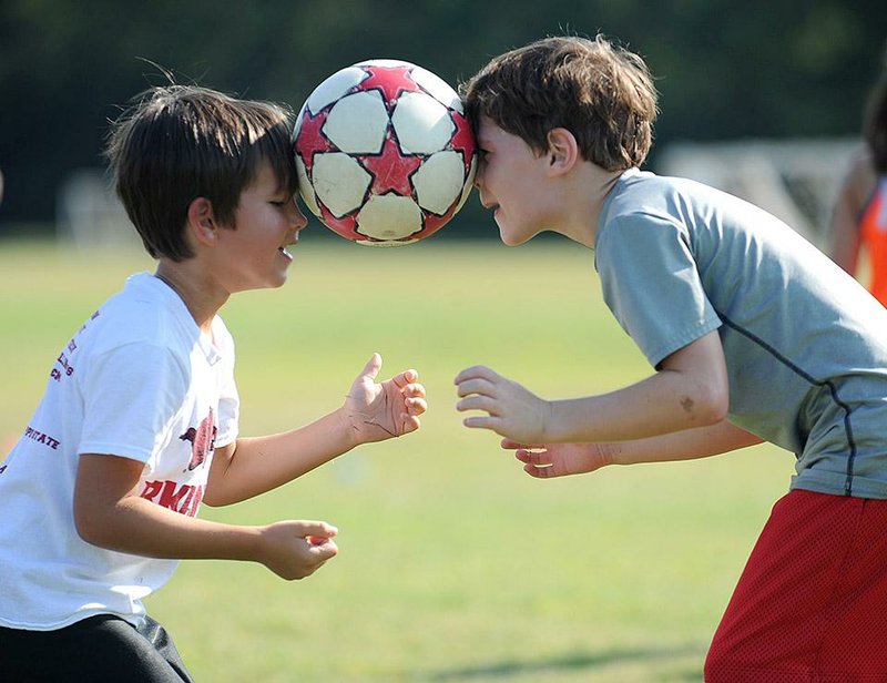 NWA Media/ANDY SHUPE - Hudson Garrett, left, and Chandler Kemp, both 6-year-olds from Fayetteville, laugh as they attempt to lower themselves to the ground with a soccer ball held between their heads while attending the Oliver Soccer Camp Tuesday, July 22, 2014, at the Lewis Soccer Complex in Fayetteville. The weeklong skills camp is meant for players 5-12 and is a part of Fayetteville high school soccer coach Steve Oliver's World Cup Summer Soccer Series that continues through Aug. 13.